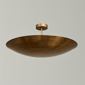 Pode incluir: Uma luminária de teto em tom de latão com uma cúpula rasa em forma de tigela. A cúpula tem pequenas perfurações espaçadas uniformemente. A luminária inclui uma haste central e uma placa de montagem circular. O design é minimalista e moderno.