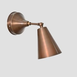Peut inclure: Une applique murale en bronze avec un abat-jour conique et un bras réglable. L'applique a une base circulaire et une finition métallique chaude. Le design est simple et moderne, adapté à divers styles d'intérieur.