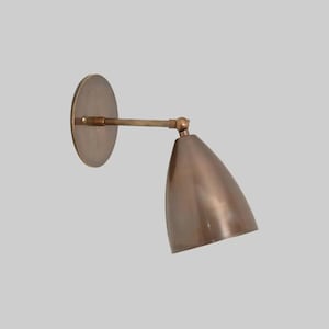 Peut inclure: Applique murale en bronze avec un abat-jour conique et une plaque arrière circulaire. La lampe a un bras pivotant pour diriger la lumière. Le luminaire en métal a un aspect vintage, idéal pour l'éclairage intérieur.