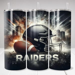 Könnte beinhalten: Ein Becher mit einem Football, Helm und dem Wort "RAIDERS" vor einer Stadtkulisse. Das Design ist überwiegend schwarz, grau und braun, mit einem silbernen Deckel und Strohhalm.