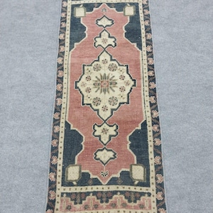 Puede incluir: Una alfombra rectangular tipo pasillero con un medallón central de color crema con motivos florales sobre un fondo rosa empolvado. La alfombra está enmarcada por un borde gris oscuro con patrones florales repetitivos y flecos cortos.