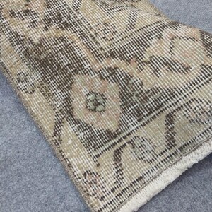 May include: A rolled-up, rectangular rug with a detailed, faded floral pattern. The rug features a color palette of beige, brown, and cream, with a fringed edge. The design appears to be vintage or antique.