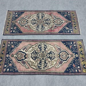 May include: Two rectangular rugs with a central medallion design. The rugs feature a pink field, navy blue borders, and intricate patterns in cream, brown, and green. The rugs have a traditional, oriental style.