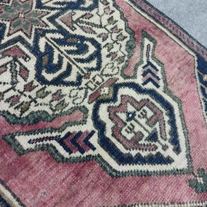 May include: Close-up of a section of a vintage rug with a detailed geometric pattern. The rug features a central design in cream, navy blue, and muted red hues. The border is navy blue with small floral motifs. The rug's texture is visible.