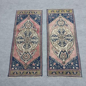 May include: Two rectangular rugs with detailed geometric patterns. The rugs have a central medallion design in cream and brown, framed by a pink border and navy blue corners. The rugs are approximately 91 cm long.