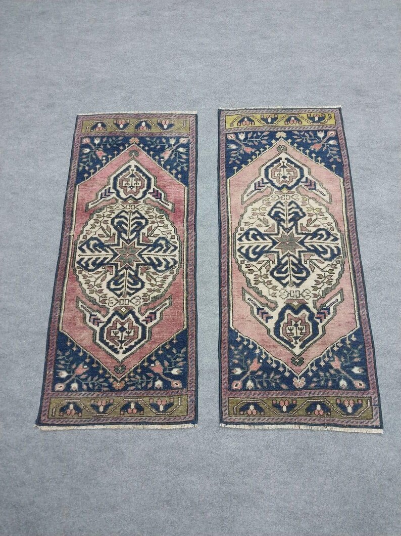 May include: Two rectangular rugs with detailed geometric patterns. The rugs have a central medallion design in cream and brown, framed by a pink border and navy blue corners. The rugs are approximately 91 cm long.