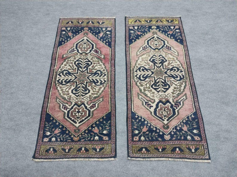 May include: Two rectangular rugs with detailed patterns. Each rug has a central design in cream, pink, and navy blue, framed by a navy border with floral details. The rugs have a traditional, vintage style.