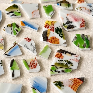 Puede incluir: Una colección de fragmentos de cerámica rotos con fondos blancos y diseños pintados a mano en verde, azul, naranja y negro. Las piezas muestran varios patrones, incluyendo estructuras arquitectónicas, follaje y trazos de pincel abstractos.
