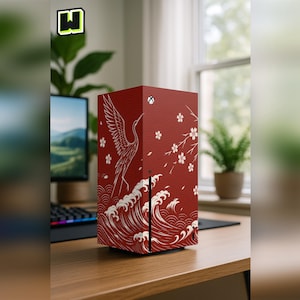 Puede incluir: Una consola roja con un diseño de inspiración japonesa que presenta una grulla, flores de cerezo y olas. La consola está decorada con detalles en blanco y dorado. La consola está sobre un escritorio de madera.