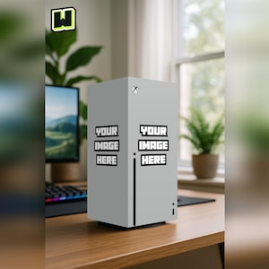 Puede incluir: Una consola rectangular gris claro con el texto "YOUR IMAGE HERE" repetido dos veces. La consola tiene una franja vertical negra y un pequeño indicador de encendido. El fondo incluye un monitor de ordenador, un teclado y una ventana.