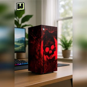 May include: A black gaming console featuring a custom skin with a dark, textured red skull graphic. The design includes glowing red eye sockets and a jagged, distressed aesthetic. The console has a white circular power button at the top center.
