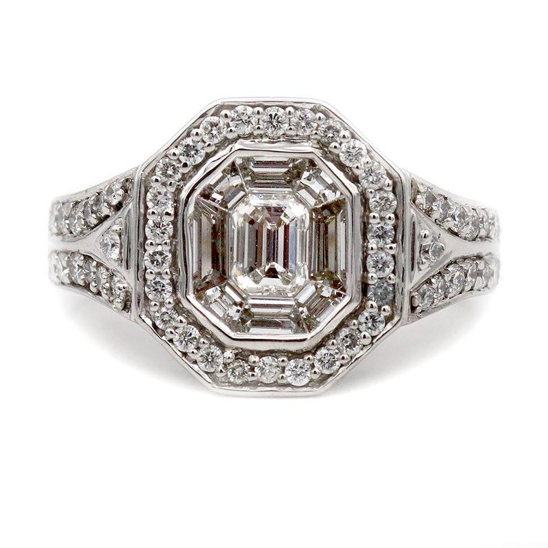 Pu&ograve; includere: Un anello color argento con un diamante centrale taglio smeraldo circondato da un alone di diamanti rotondi pi&ugrave; piccoli. La fascia &egrave; divisa in due sezioni su ciascun lato, con ulteriori diamanti rotondi incastonati sulla superficie.