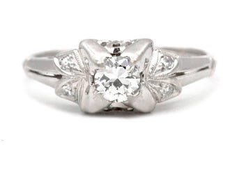 May include: A vintage platinum engagement ring with a round brilliant cut diamond center stone and smaller diamonds set in a delicate floral design.