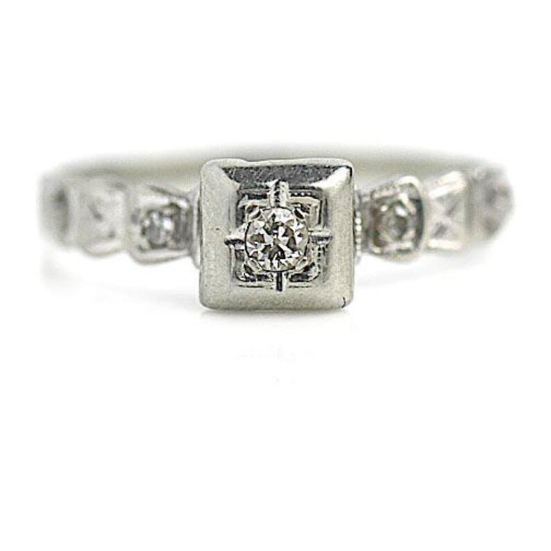 May include: A silver ring with a square-shaped center stone and smaller stones on the band.