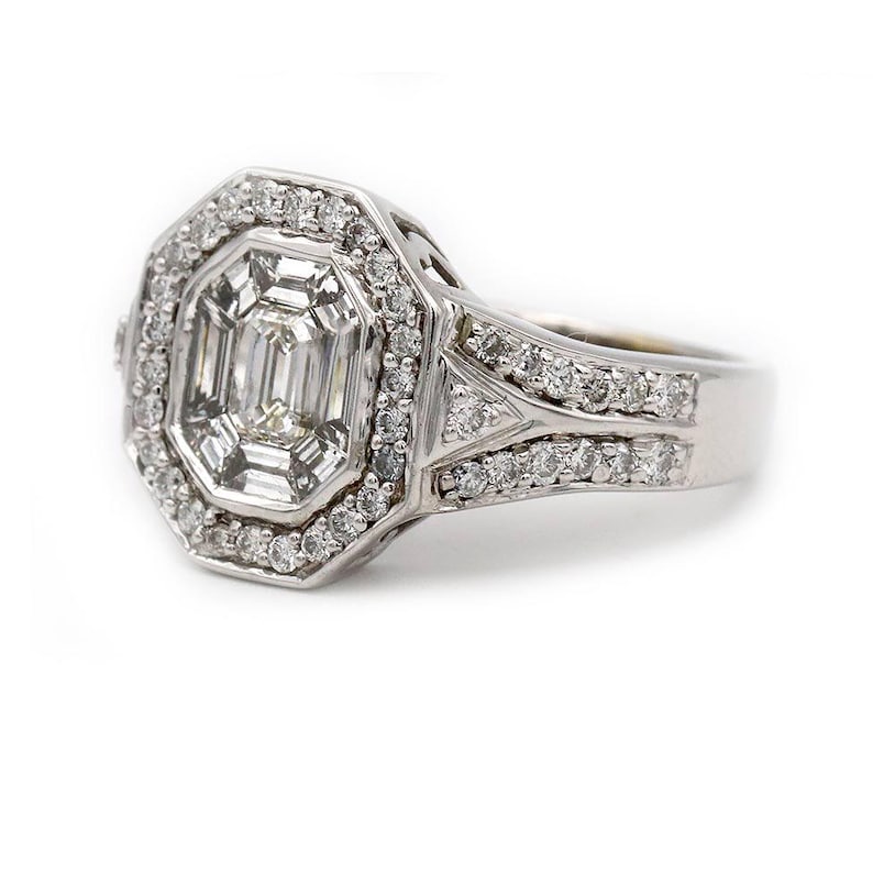 Pu&ograve; includere: Un anello color argento con una pietra centrale taglio smeraldo circondata da un alone di piccole pietre rotonde. La fascia &egrave; divisa in due file di pietre incastonate a pav&eacute; che si incontrano sui lati, creando una cornice ottagonale.