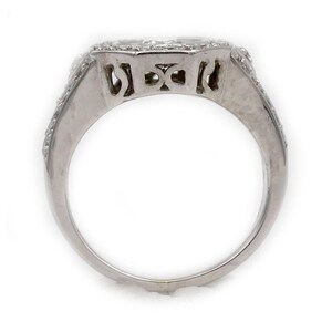 Pu&ograve; includere: Un anello color argento con una fascia larga e un intricato design traforato. La parte superiore dell'anello &egrave; incastonata con molteplici piccole pietre chiare e scintillanti disposte in un motivo geometrico che si estende lungo i lati.
