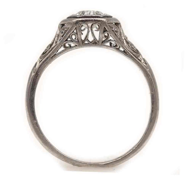 Puede incluir: Un anillo de compromiso de filigrana de plata con un diamante redondo y claro en el centro.