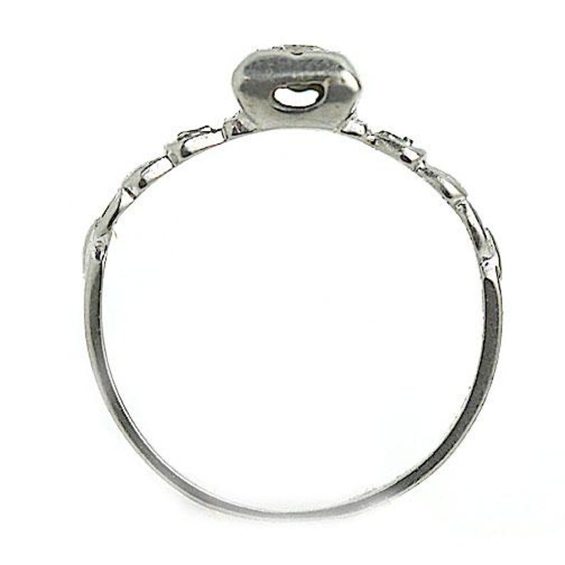 May include: A silver ring with a delicate design and a small, clear stone in the center.