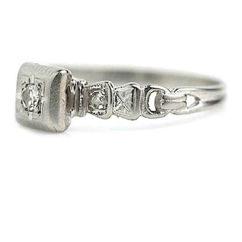 May include: A silver ring with a square-shaped diamond set in a bezel setting. The band is decorated with a repeating pattern of small diamonds.