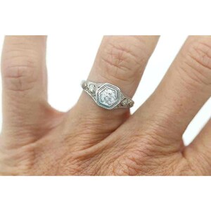Puede incluir: Un anillo de plata con una piedra central hexagonal y piedras de acento m&aacute;s peque&ntilde;as. El anillo est&aacute; en un dedo.