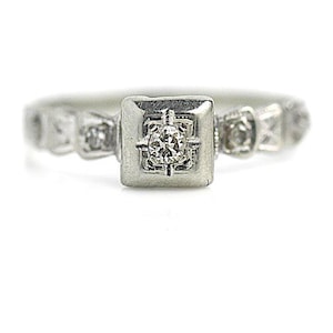 May include: A silver ring with a square-shaped center stone and smaller stones on the band.