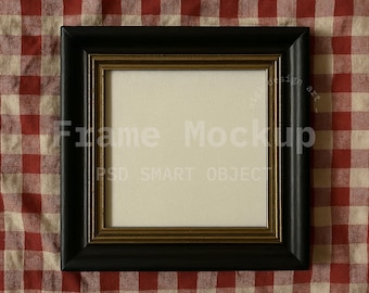 May include: A square black picture frame with a gold inner border, set against a red and white checkered background. The frame has the words "Frame Mockup" and "PSD SMART OBJECT" printed on it.