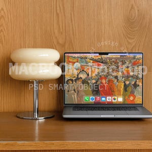 May include: A modern desk setup featuring a laptop displaying a colorful painting and a cream-colored, double-layered lamp. The lamp has a chrome base. The desk and background are made of wood. The laptop screen shows the text "PSD SMART OBJECT".