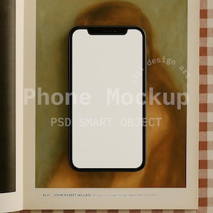 Puede incluir: Un teléfono inteligente negro con una pantalla blanca en blanco está centrado en una página con el texto "Phone Mockup" y "PSD SMART OBJECT". La página está abierta sobre una mesa con un patrón a cuadros marrón y blanco.