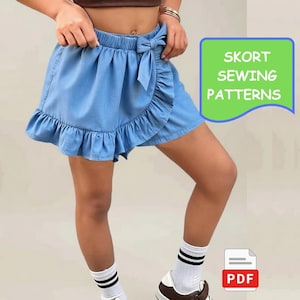 Puede incluir: Una falda pantalón azul claro estilo mezclilla con cintura elástica, un lazo decorativo en la parte delantera, un diseño cruzado y un dobladillo con volantes. La imagen incluye texto verde que dice SKORT SEWING PATTERNS y un icono PDF.