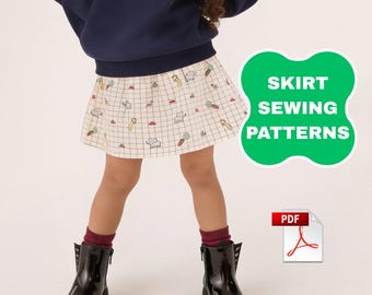 May include: A skirt with a white grid pattern featuring small colourful illustrations of cats, carrots, and other items. The image includes a green badge with the text SKIRT SEWING PATTERNS and a PDF file icon. The skirt is worn with a dark blue sweater.