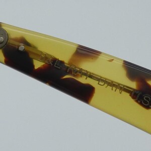 May include: Close-up of a portion of a pair of eyeglasses. The frame is a light yellow with brown tortoise shell patterns. The text "B&L RAY-BAN U.S.A." is visible on the arm of the glasses.