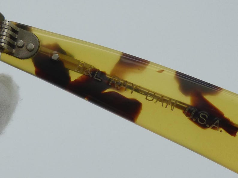 May include: Close-up of a portion of a pair of eyeglasses. The frame is a light yellow with brown tortoise shell patterns. The text "B&L RAY-BAN U.S.A." is visible on the arm of the glasses.