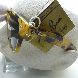 May include: Tortoiseshell Ray-Ban sunglasses with dark lenses. The sunglasses have a classic design with the Ray-Ban logo on the temple and a tag with the Ray-Ban logo and "INTENSITY LENSES" printed on it.