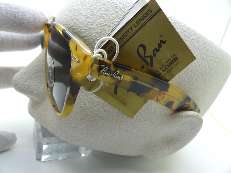 May include: Tortoiseshell Ray-Ban sunglasses with dark lenses. The sunglasses have a classic design with the Ray-Ban logo on the temple and a tag with the Ray-Ban logo and "INTENSITY LENSES" printed on it.
