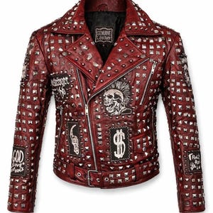 Front view of a red studded leather jacket featuring silver pyramid studs across the collar, shoulders, and body, with skull patches and an asymmetrical biker zipper on a clean white background.