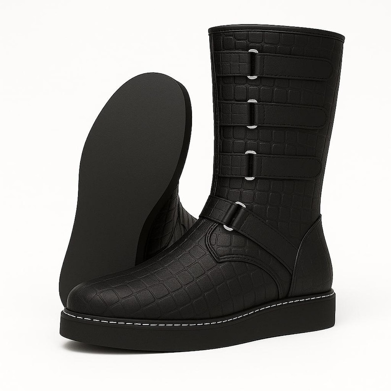 May include: Black leather boots with a textured, crocodile-like pattern. The boots have a mid-calf height, a thick sole with white stitching, and multiple straps with silver buckles. One boot is upright, and the other is lying on its side.