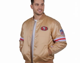 May include: A gold satin bomber jacket with the San Francisco 49ers logo on the chest and NFL logo on the sleeve. The jacket has red and white stripes on the sleeve cuffs and a brown ribbed collar and hem.