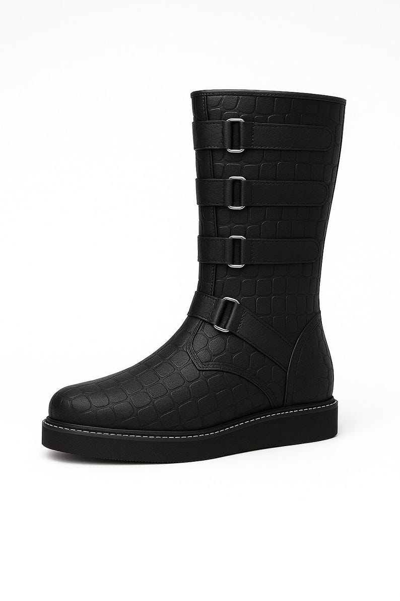 May include: Black mid-calf boot with a textured, crocodile-like pattern. The boot features three straps with silver buckles and a fourth strap at the ankle. The sole is black with white stitching.