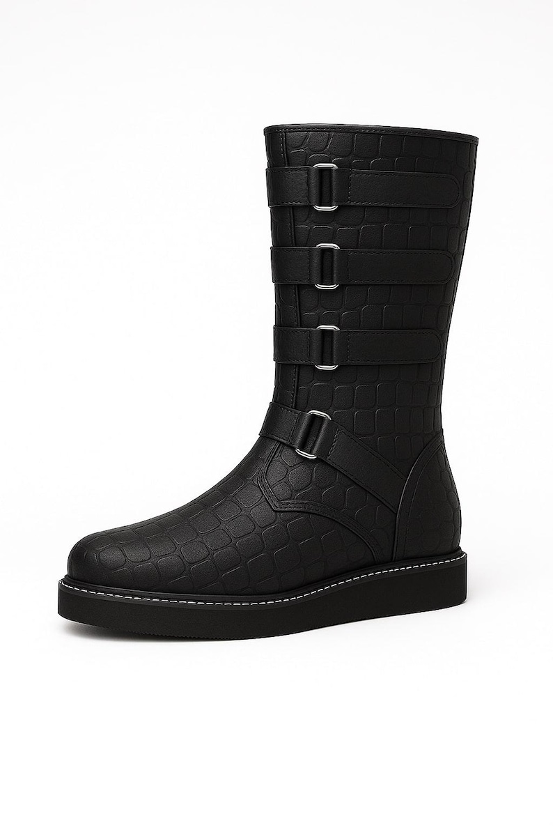 May include: Black mid-calf boot with a textured, crocodile-like pattern. The boot features three straps with silver buckles and a fourth strap at the ankle. The sole is black with white stitching.