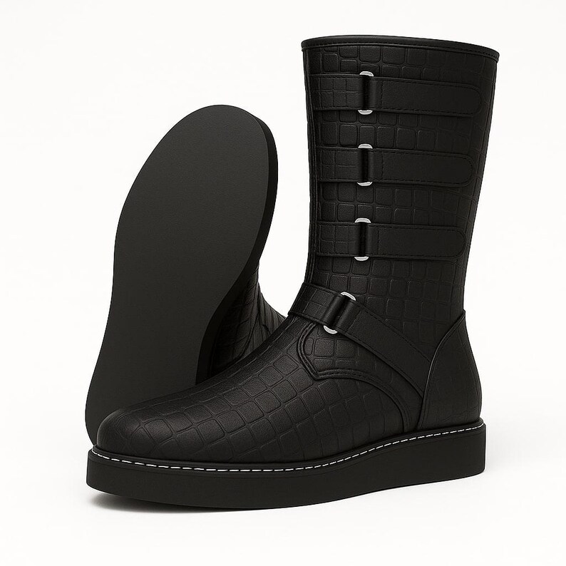 May include: Black leather boots with a textured, crocodile-like pattern. The boots have a mid-calf height, a thick sole with white stitching, and multiple straps with silver buckles. One boot is angled to show the sole.