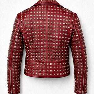 Detailed close-up of embroidered skull patch stitched onto red leather jacket surrounded by metal studs and rivets.