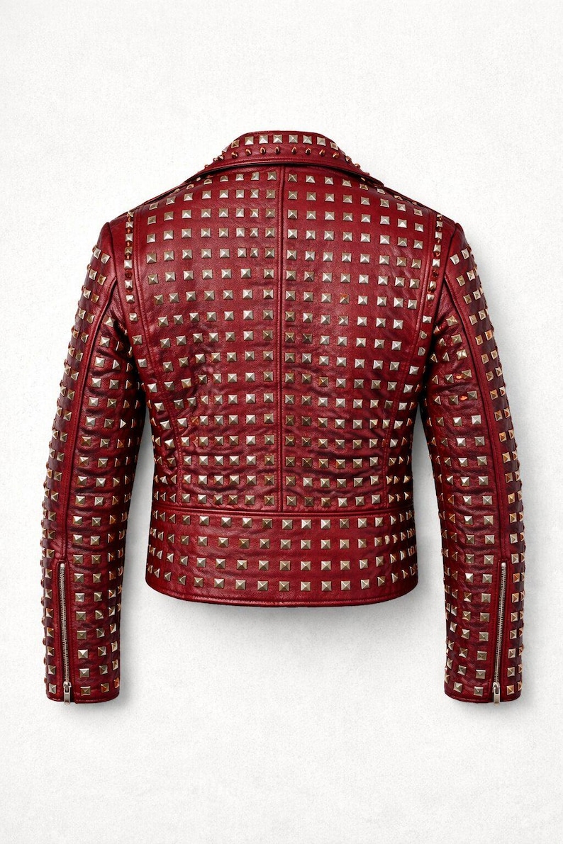 Detailed close-up of embroidered skull patch stitched onto red leather jacket surrounded by metal studs and rivets.