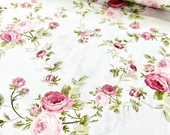 Op de afbeelding: Witte stof met een bloemenpatroon van roze rozen en groene bladeren. De rozen variëren in grootte en tint, sommige zijn volledig in bloei en andere in knopvorm. Het ontwerp is verdeeld over de stof.