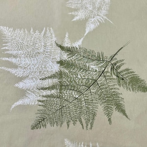 Puede incluir: Primer plano de una tela con un patrón repetido de hojas de helecho. Las hojas son en tonos blancos y verdes, sobre un fondo beige claro. El diseño tiene un tema natural y botánico.