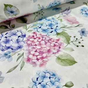 Puede incluir: Tela blanca con un estampado floral de acuarela con flores de hortensia azules, moradas y rosas. Hojas verdes y flores azules y moradas más pequeñas están dispersas por la tela. La tela está enrollada en la esquina superior izquierda.