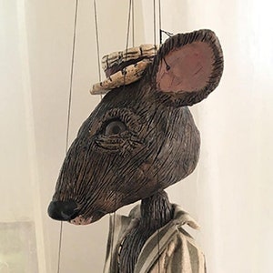 May include: A brown and tan puppet of a mouse wearing a striped jacket, brown pants, and a hat. The puppet has a long, segmented tail.