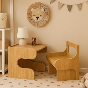Puede incluir: Un juego de mesa y silla para niños de madera clara. La mesa tiene un diseño curvo único. Un pequeño oso de peluche está sentado en la mesa. También se ve un adorno de pared de león y una lámpara pequeña.