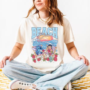 A woman wearing a white t-shirt with a graphic design of a beach scene and cartoon characters.
