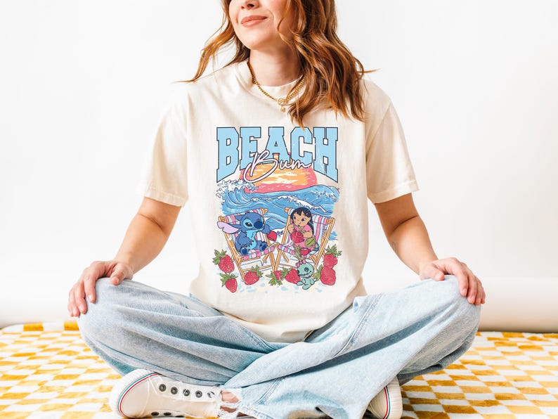 A woman wearing a white t-shirt with a graphic design of a beach scene and cartoon characters.