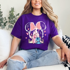 A woman wearing a purple t-shirt with a Disney-themed graphic is sitting on a couch, smiling.